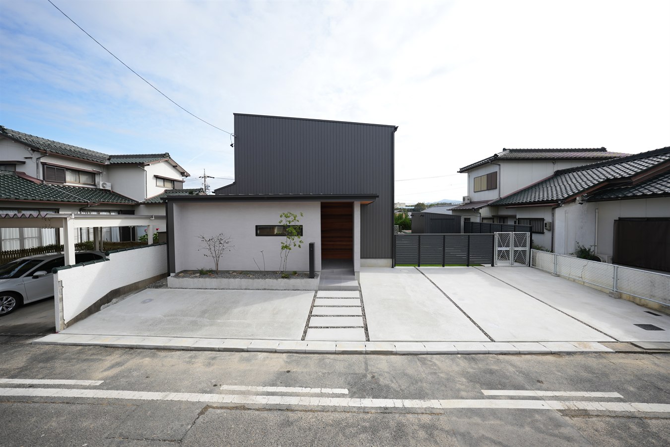 住宅地に建つ注文住宅の外観。白い1階の上に一回り小さい黒いガルバリウムの2階が載る部分2階の構成